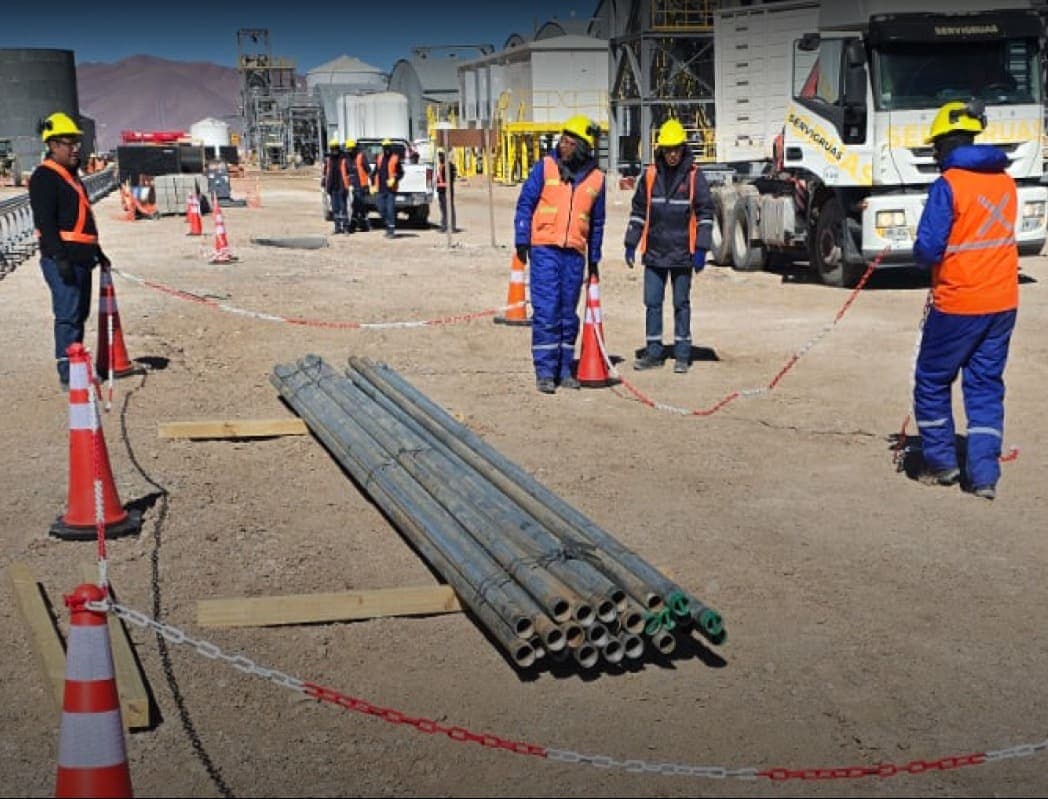 Cañerías de acero y camión grúa en un obrador minero con operarios y conos de señalización