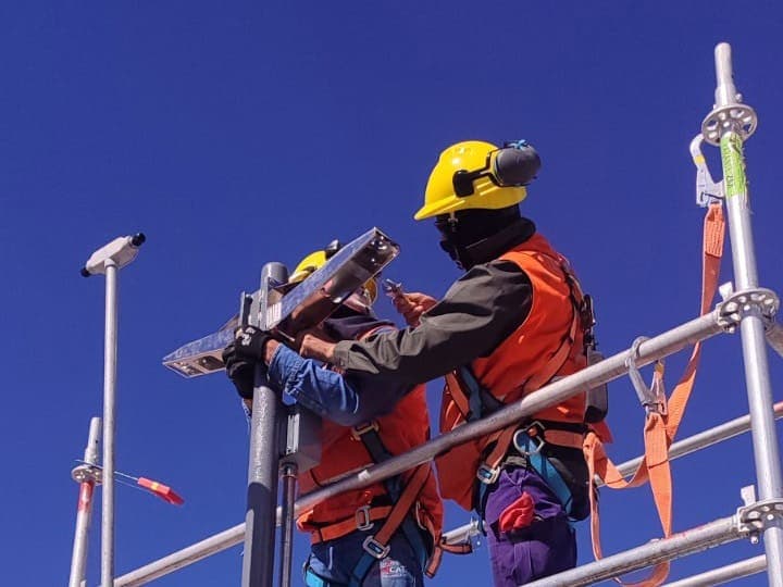 Operarios en andamio montando cámaras sobre postes contra un cielo despejado