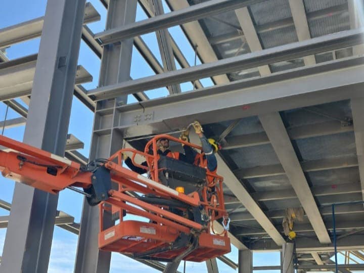 Operario en plataforma elevadora trabajando sobre la estructura de acero de una nave industrial