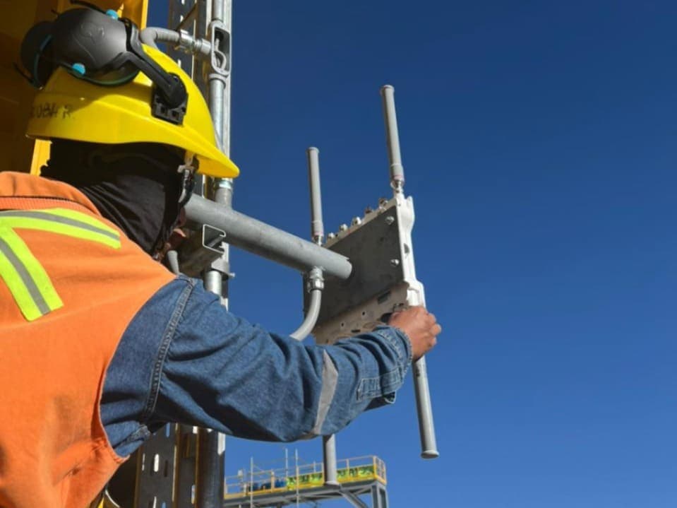 Operario instalando un panel de antena en un mástil contra el cielo