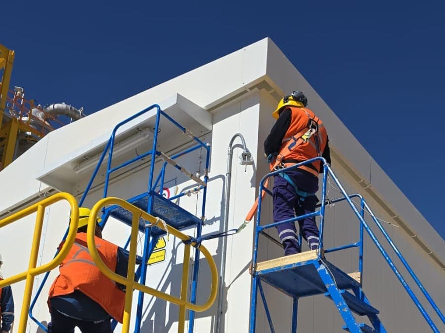 Operarios en andamio instalando cañería sobre la fachada de un edificio industrial